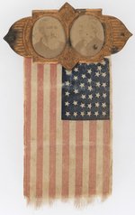 HARRISON & MORTON 1888 BRASS SHELL JUGATE BADGE W/AMERICAN FLAG RIBBON.